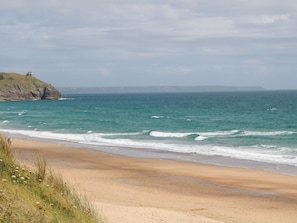Une plage bordée d’une falaise rocheuse, avec un phare en arrière-plan.
