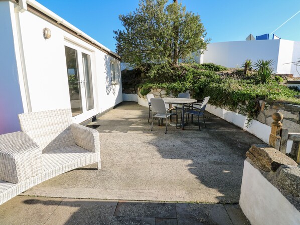 A patio with a white wicker sofa, a round table with chairs, and a stone wall. - Salakee (Penzance)