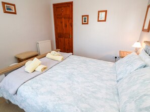 A neatly made bed with towels, a wooden door, and a small bedside table with a lamp. - Salakee (Penzance)