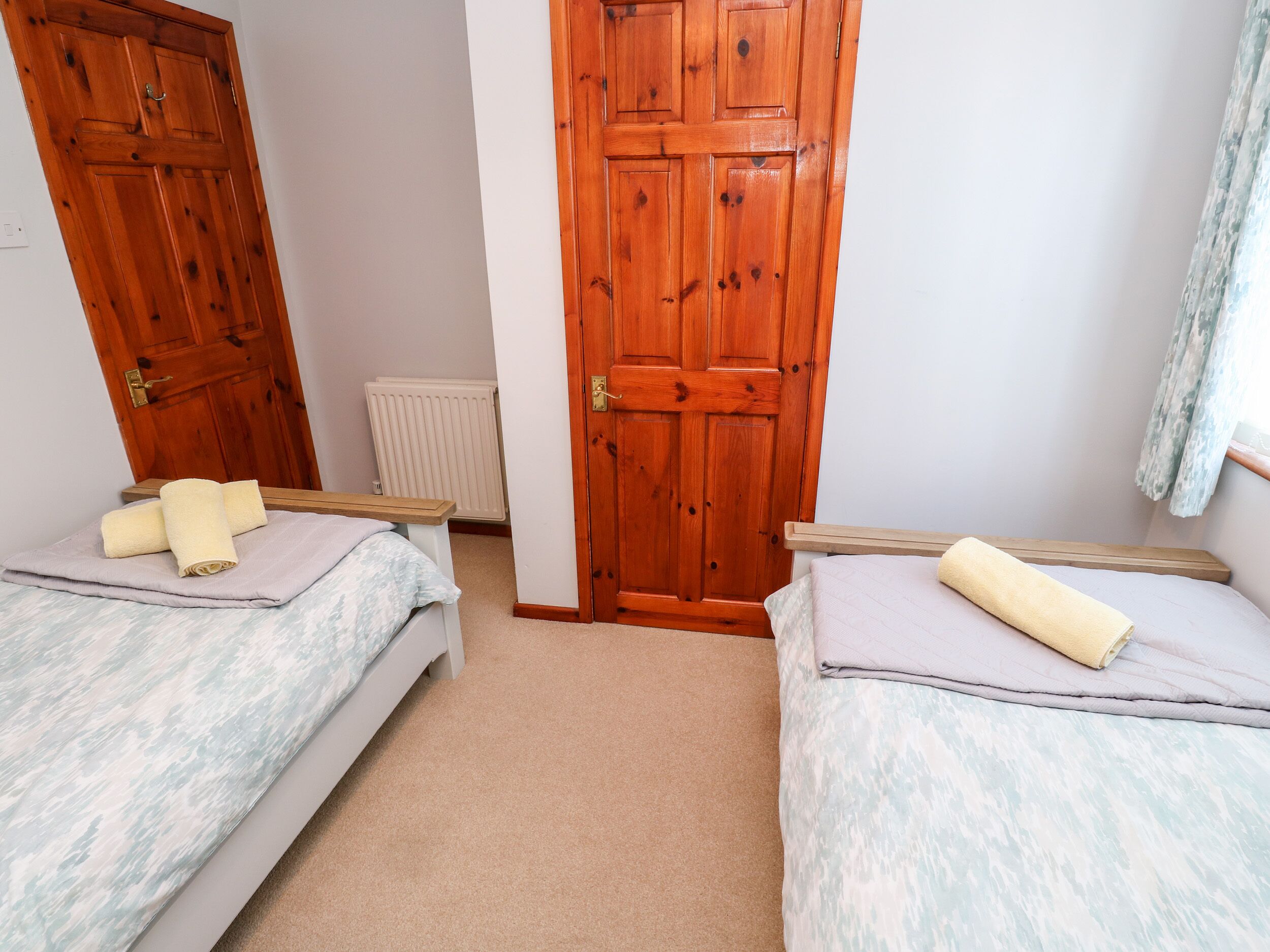 A bedroom with two single beds, wooden doors, a radiator, and a window with a curtain.