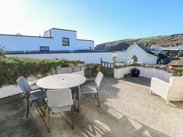 Une terrasse avec une table ronde et des chaises, un mur en pierre et une vue sur un bâtiment blanc et des collines en arrière-plan.