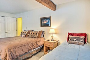 A bedroom with two beds, a nightstand with a lamp, a framed picture on the wall, and a door leading to another room. - 1 Mi to Attitash Mountain: Condo w/ Resort Perks (Bartlett)