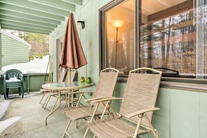 A covered patio with wicker chairs and a table, a window with a lamp, and a green door. - 1 Mi to Attitash Mountain: Condo w/ Resort Perks (Bartlett)