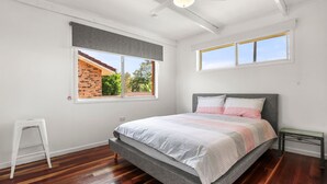 Une chambre à coucher avec un lit, deux fenêtres, une petite table et une chaise blanche.