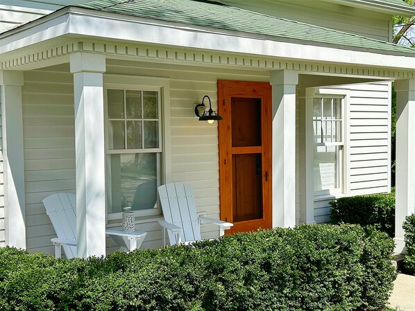 Een wit huis met een veranda, een houten deur en twee witte stoelen.