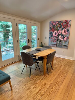 Een eetgedeelte met een houten tafel en stoelen, een schilderij aan de muur en een uitzicht door glazen deuren op een terras.
