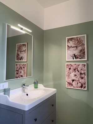 A bathroom with a white sink, a mirror, and three framed floral photographs on the wall.