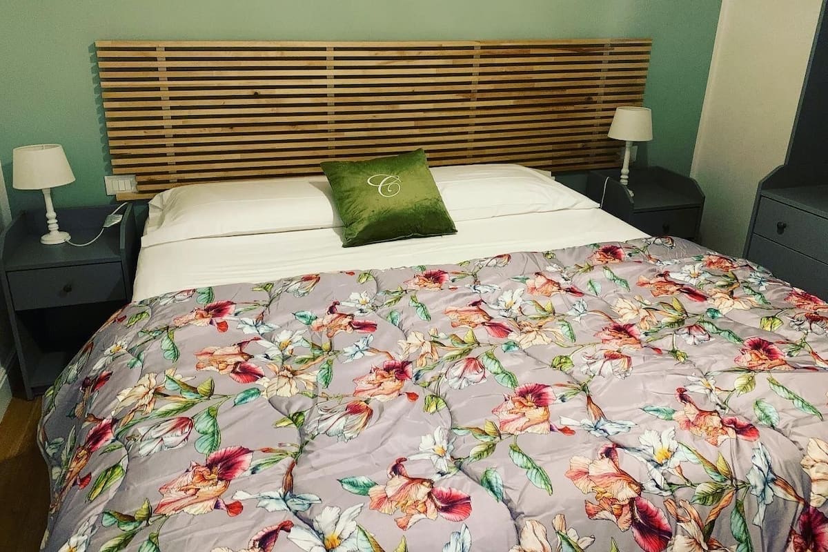 A bed with a floral duvet, a wooden headboard, two bedside tables with lamps, and a green pillow.