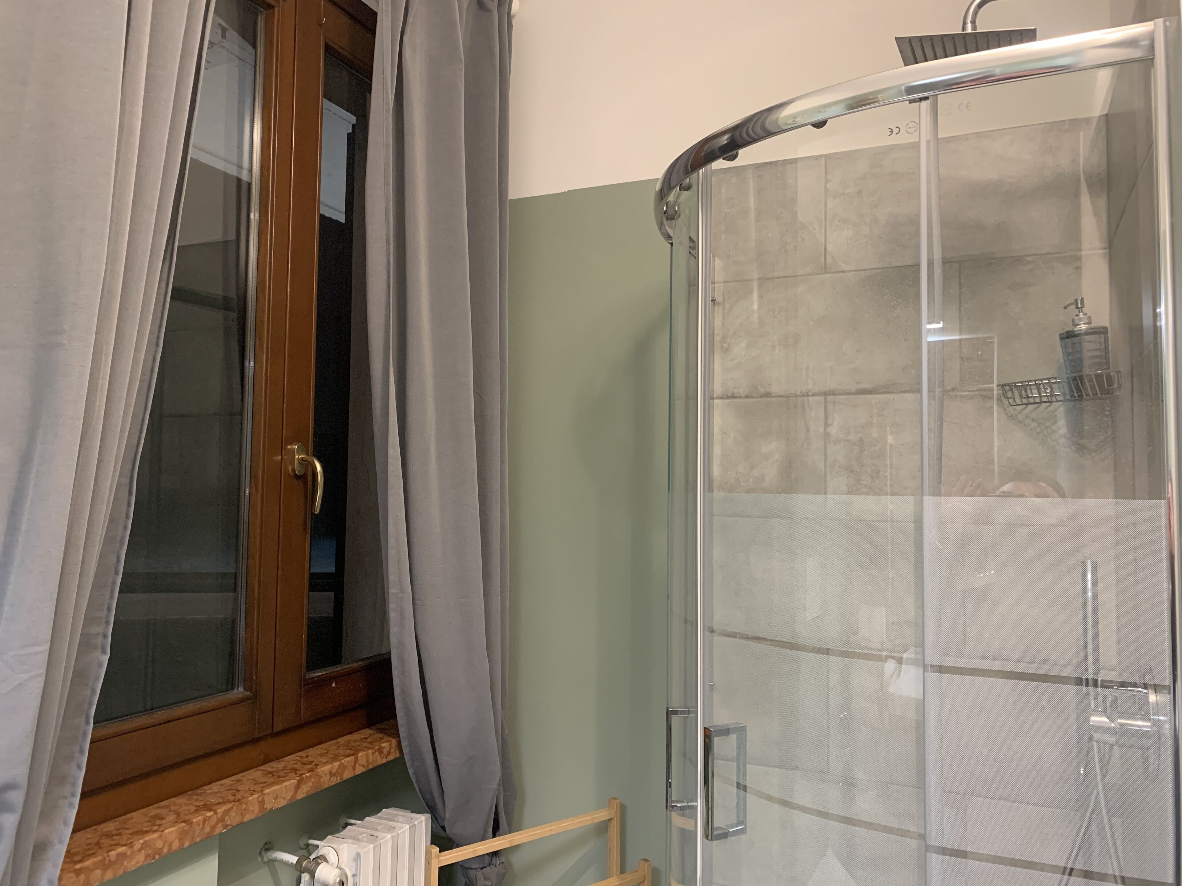 Une salle de bain avec une douche à parois de verre, une fenêtre avec des rideaux et un porte-serviettes.