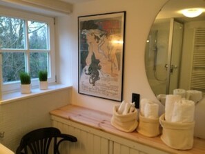 A bathroom with a window, a radiator, a chair, and towels on the counter.