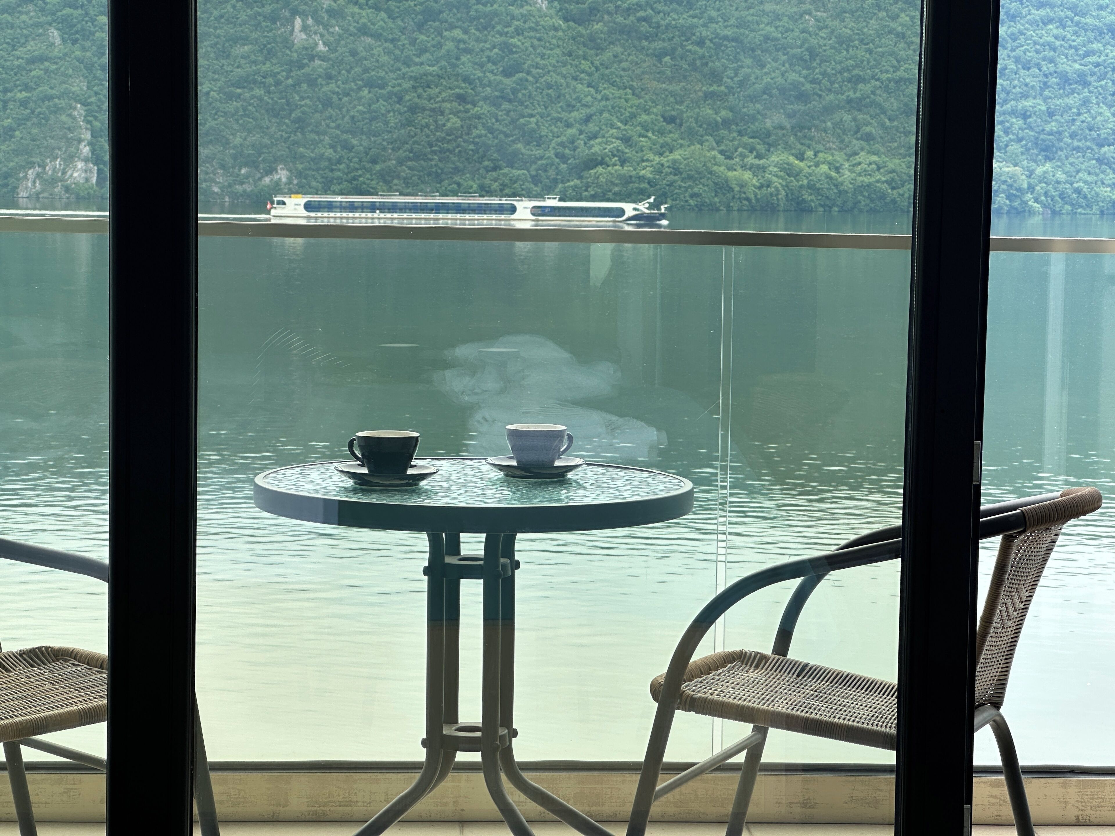 A balcony with a table and chairs overlooking a body of water and a forested hillside.