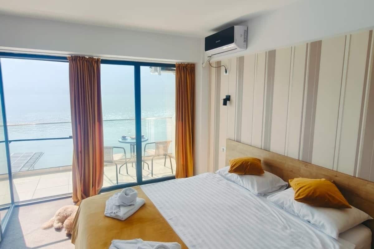 Ein Hotelzimmer mit Bett, Meerblick, einem Balkon mit Stühlen und einer Klimaanlage.