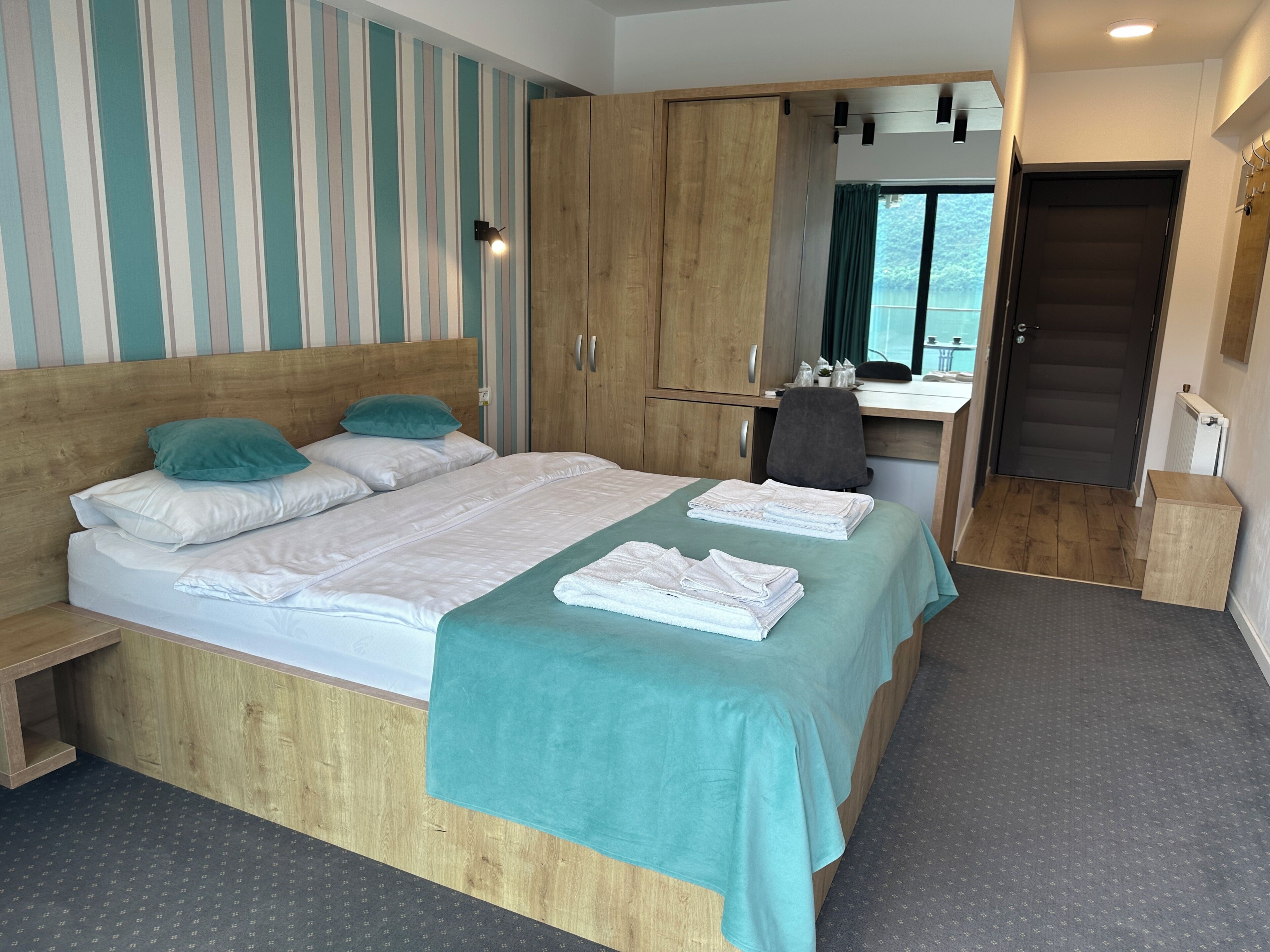 A hotel room with a bed, a desk, a wardrobe, and a view of the outdoors.
