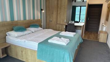 A hotel room with a bed, a desk, a wardrobe, and a view of the outdoors.