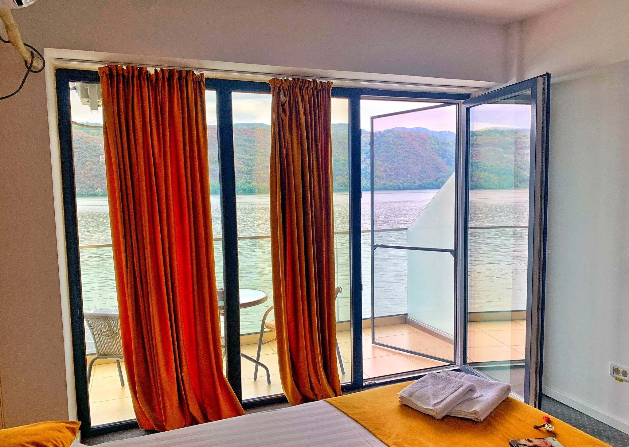 A room with a bed, a table, and a view of a lake and mountains.