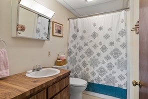 A bathroom with a wooden vanity, a white sink, a toilet, and a shower curtain with a geometric pattern.