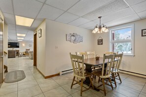 A dining area with a wooden table and chairs, a ceiling light fixture, and a window with a view of trees.