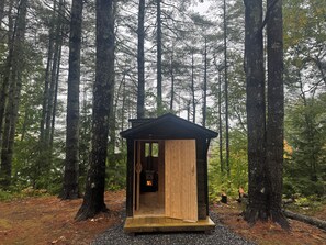 A small wooden cabin with a sloped roof, situated in a forest with tall trees.