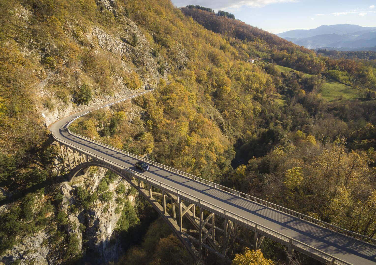 A bridge with a single lane in each direction, surrounded by forested hills and a clear sky.