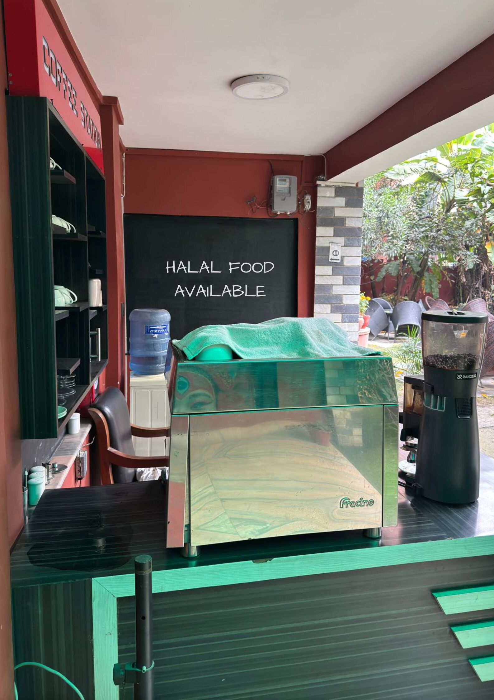 Una cafetería con un letrero que indica la disponibilidad de comida halal, un área de descanso con sillas y mesas, y un dispensador de agua.