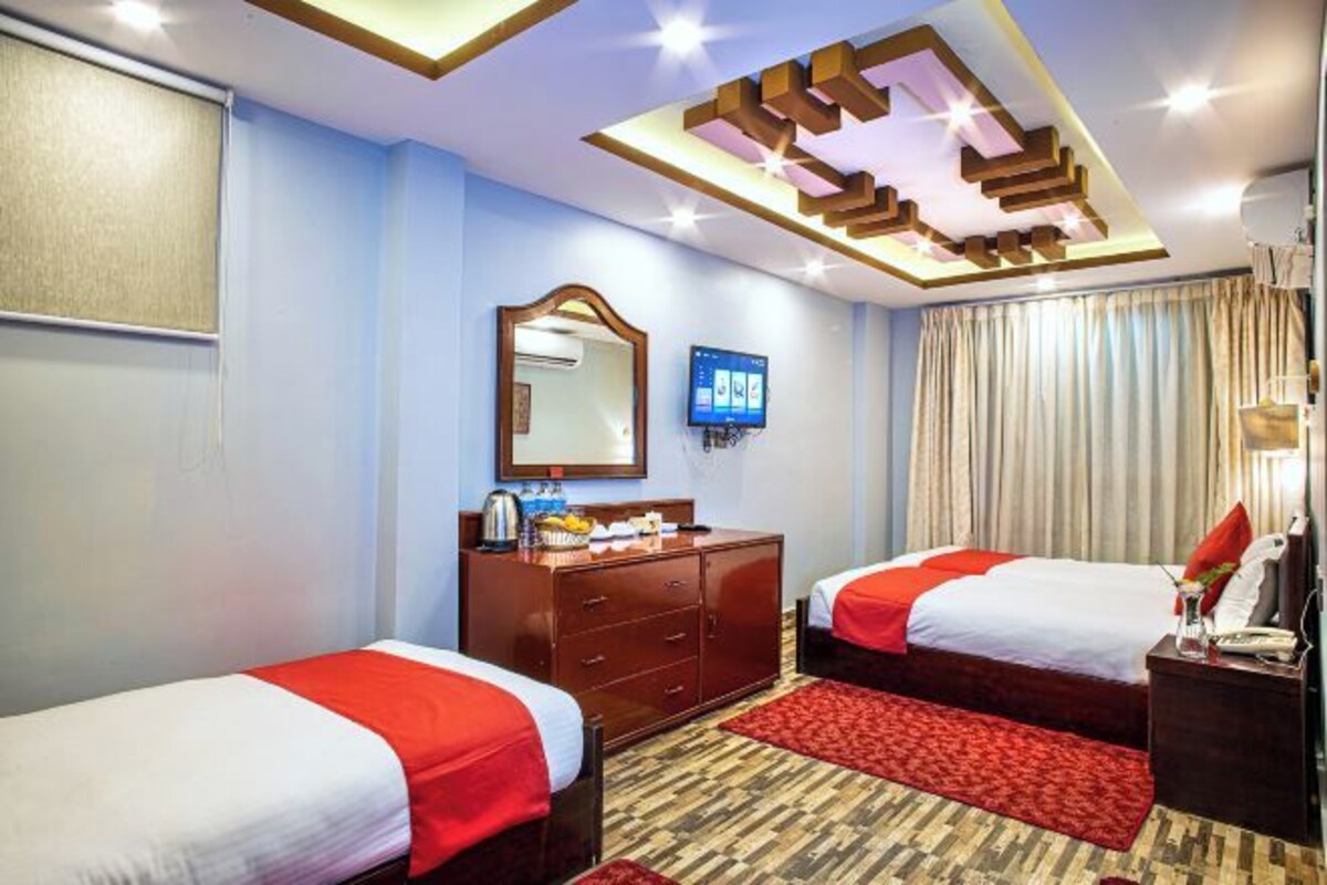 A hotel room with two beds, a wooden dresser, a mirror, a television, and a red carpet.