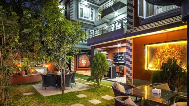 An outdoor patio area with wicker furniture, a small garden, and a mural on the wall. - Hotel BnB Mhepi (Kathmandu)
