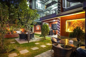 Uma área de pátio ao ar livre com móveis de vime, um pequeno jardim e um mural na parede.