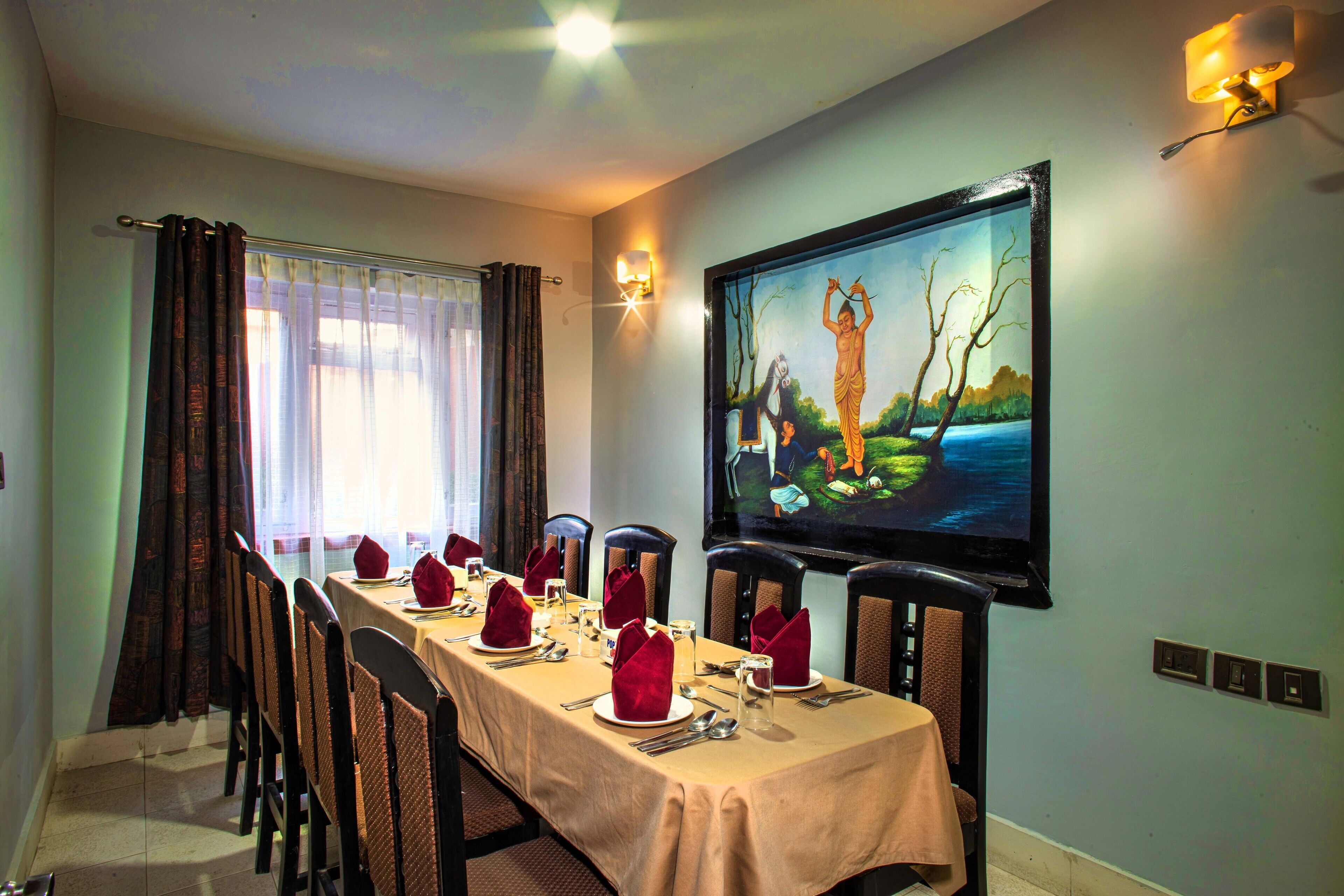 A dining room with a long table set for a meal, chairs, a painting on the wall, and a television.