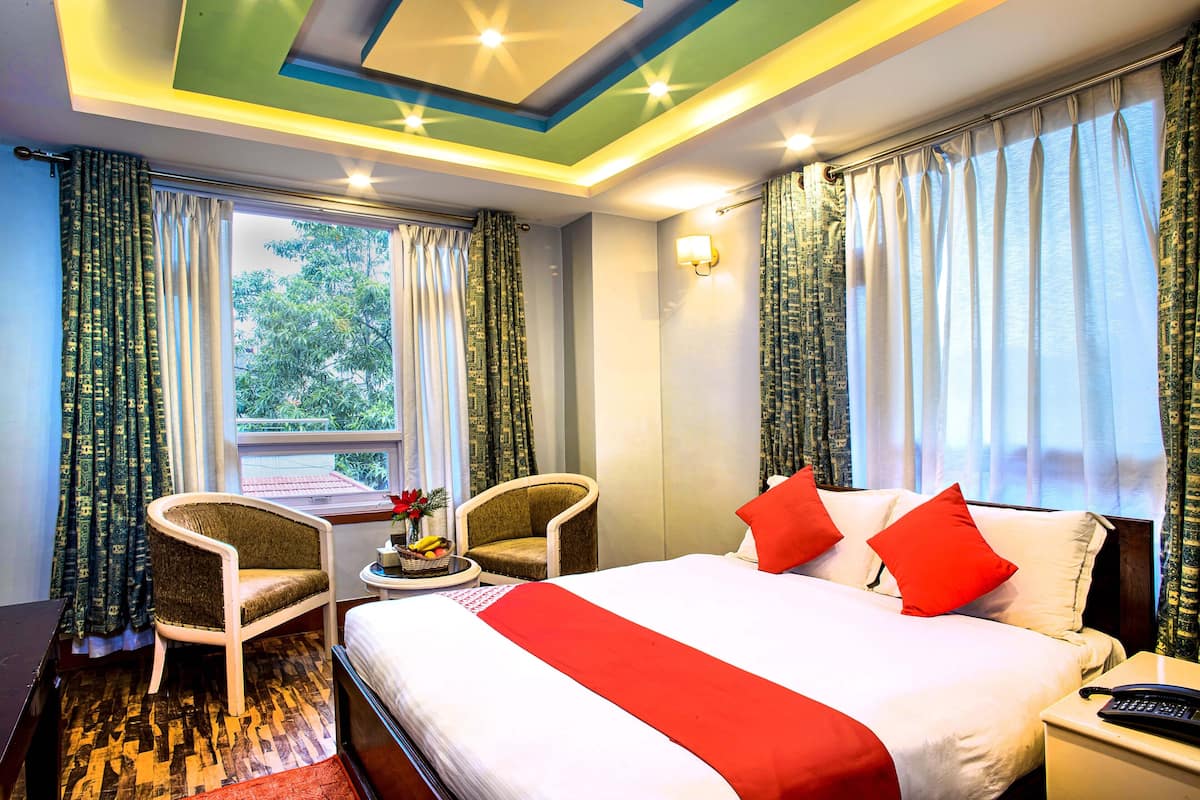 Ein Hotelzimmer mit einem Bett, zwei Sesseln, einem kleinen Tisch mit Obst und Vorhängen.