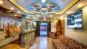 A hotel lobby with a reception desk, a sofa, a wall-mounted TV, and a decorative ceiling. - Hotel BnB Mhepi (Kathmandu)