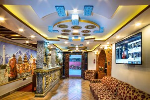 Un vestíbulo de hotel con mostrador de recepción, un sofá, un televisor montado en la pared y un techo decorativo.