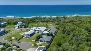 An aerial view of a coastal property with multiple buildings, a road, and a dense forest. - Beach & Boats Agnes Water (AGNES WATER)