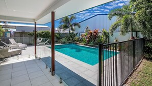 A swimming pool with a tiled deck, surrounded by a metal fence, and a covered patio area with lounge chairs. - Beach & Boats Agnes Water (AGNES WATER)