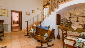 A spacious living area with a wooden rocking chair, a dining table with a vase, and a staircase leading to an upper level. - PUTXET D'EN ROBI Finca for 6 with pool in Sineu (Sineu)
