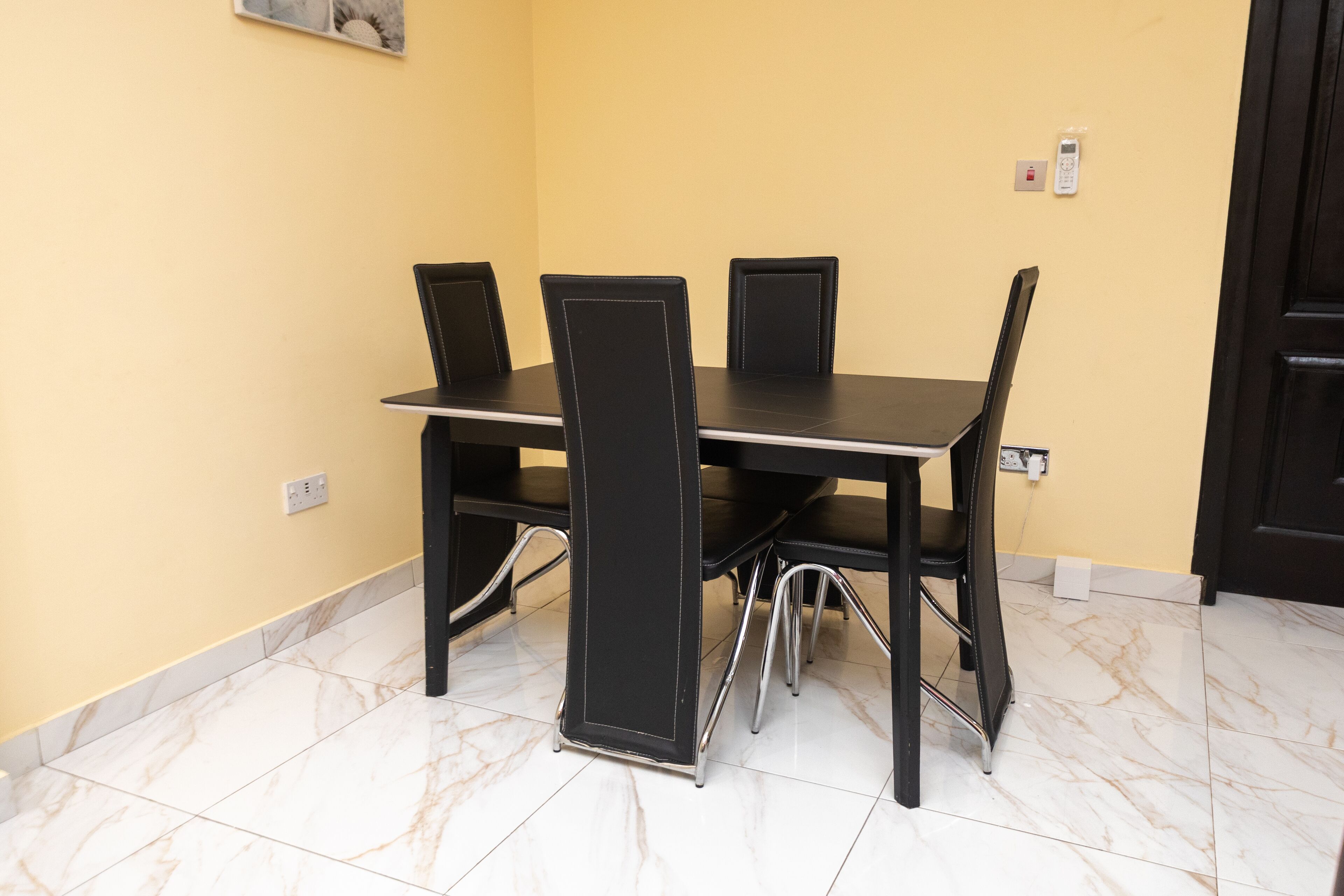 A dining area with a table and chairs, a yellow wall, and a door.