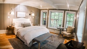 Ein Schlafzimmer mit einem großen Bett, Nachttischen, einer Bank, einem Sessel und einem Fenster mit Blick auf Grünflächen.