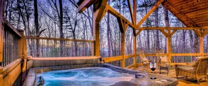 Una cabaña de madera con jacuzzi, terraza de madera y sillas con vista a un bosque.