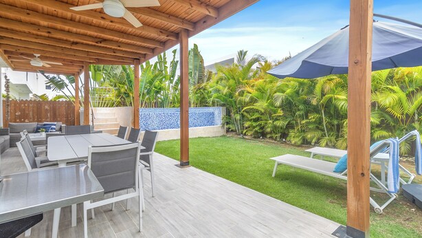 Une terrasse extérieure dotée d’une pergola en bois, un espace repas avec une table et des chaises, et un espace piscine avec des chaises longues.