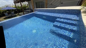 Une piscine aux carreaux de mosaïque bleus, entourée de chaises longues et de parasols.