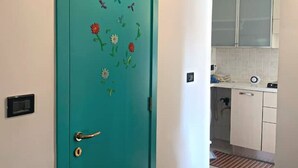Una puerta azul verdoso con diseños florales y de mariposas, que da a una cocina con armarios blancos y un ventanal sobre el lavadero.