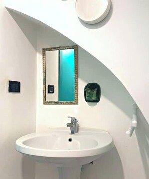 Un bagno con un lavandino bianco, uno specchio con cornice dorata e un portasapone verde.