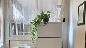 Una cocina compacta con un refrigerador blanco, un mueble pequeño blanco y una ventana con cortinas de encaje.