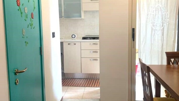 Una cocina con armarios blancos, una ventana con cortina y un comedor con mesa y sillas de madera.