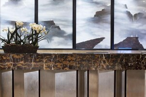 Un área de recepción con mostrador de mármol, una planta en maceta con flores blancas y vistas a formaciones rocosas a través de grandes ventanales.