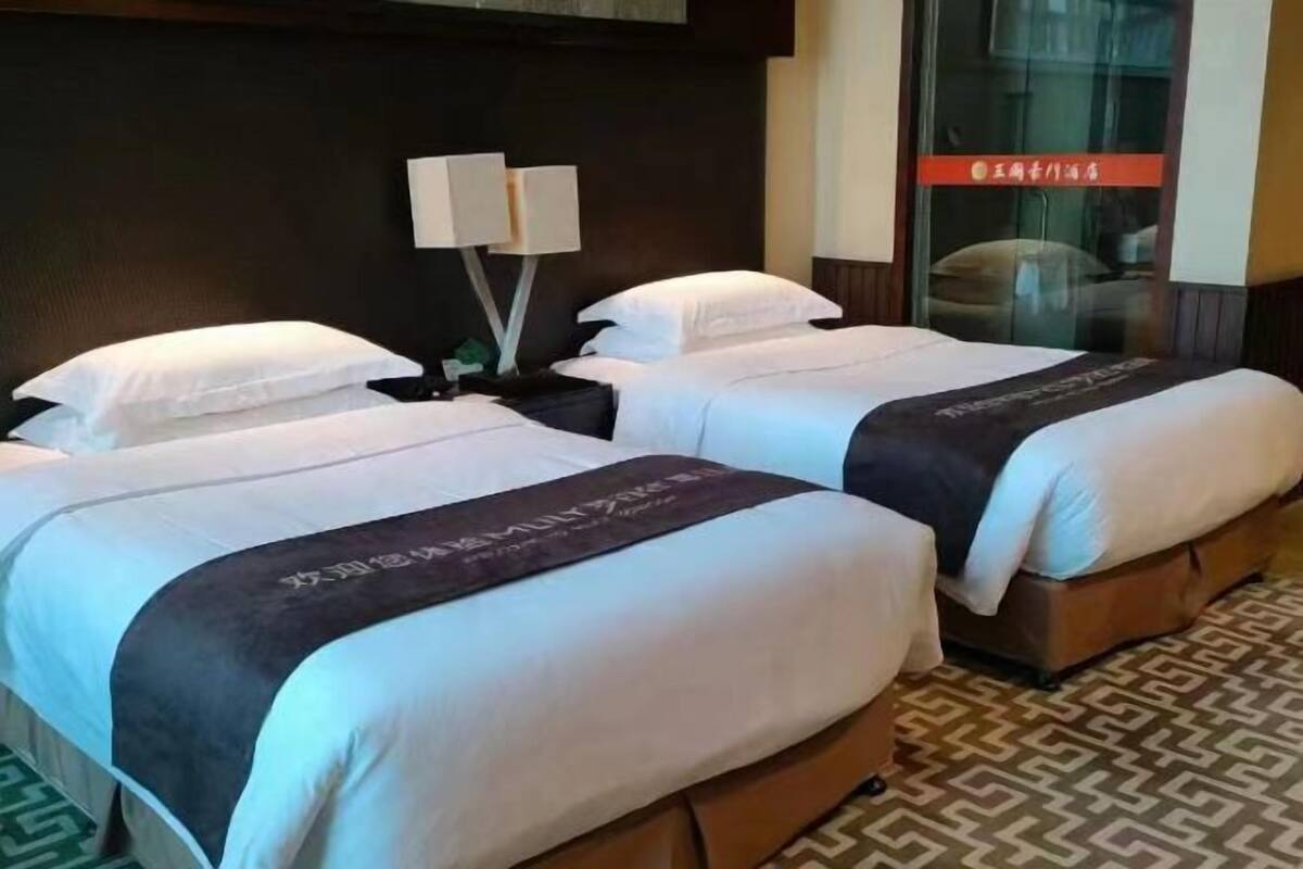 Two beds with white bedding and dark headboards, a nightstand with a lamp, and a patterned floor.