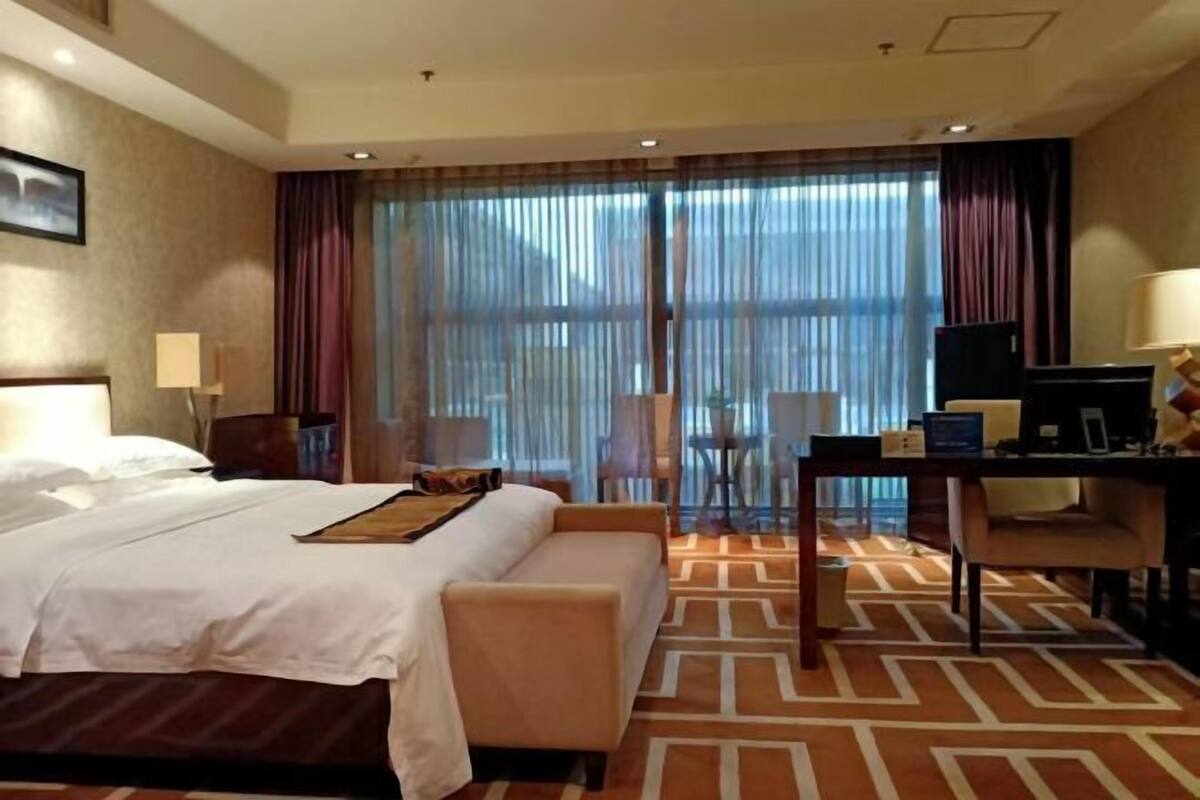 A hotel room with a bed, a desk, a chair, a TV, and a window with curtains.