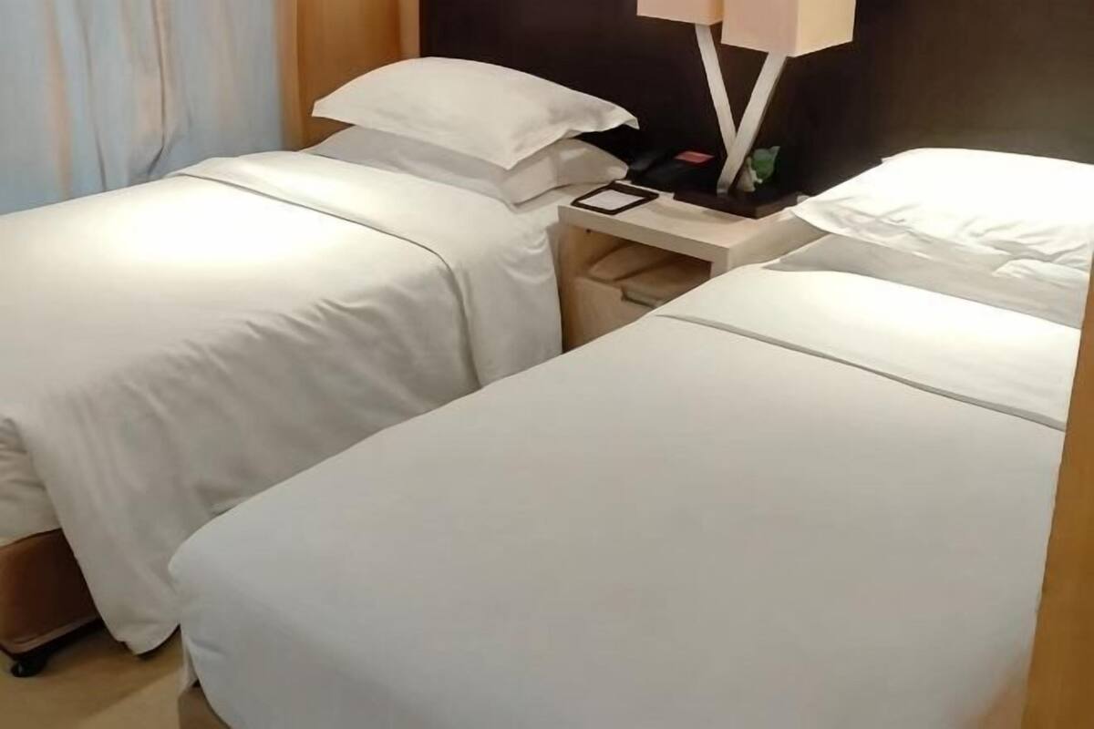 A hotel room with two single beds, a bedside table with a lamp, and a small nightstand.