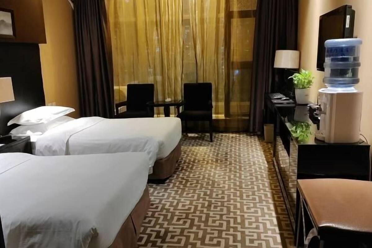 A hotel room with two beds, a desk, a chair, a water dispenser, and a lamp.