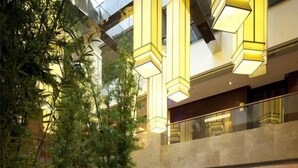 Un espacio interior de varios niveles con arquitectura moderna, que cuenta con un techo de vidrio y luminarias geométricas iluminadas.