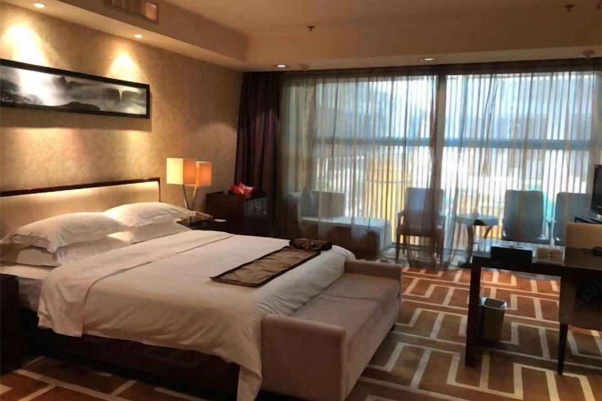 A hotel room with a large bed, a desk, a chair, and a view of the outdoors.